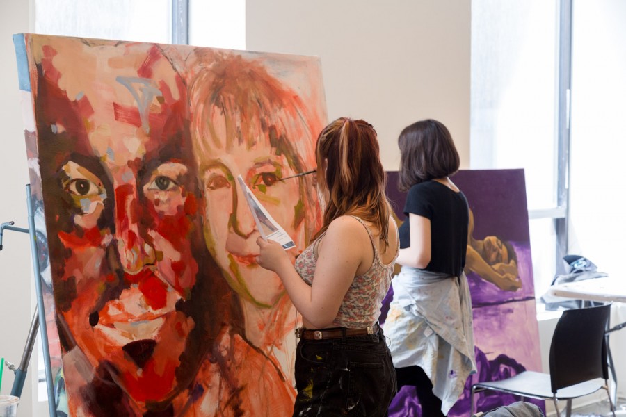 Two SVA students are working on one painting of two portraits very close to each other.