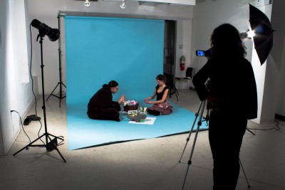Students sit down on a blue seamless background. Lighting and a camera with tripod are part of the set.