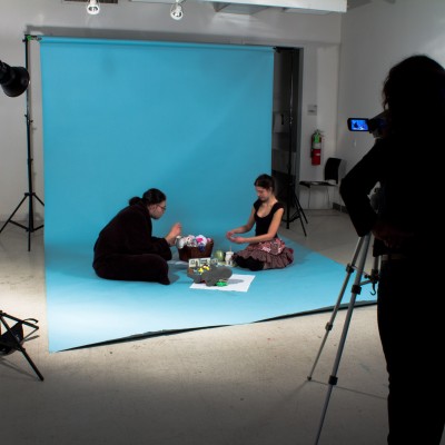 Students sit down on a blue seamless background. Lighting and a camera with tripod are part of the set.