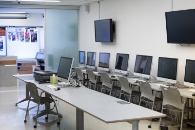 Editing classroom with multiple iMacs placed on desks. The class has access to the print room through sliding glass doors.