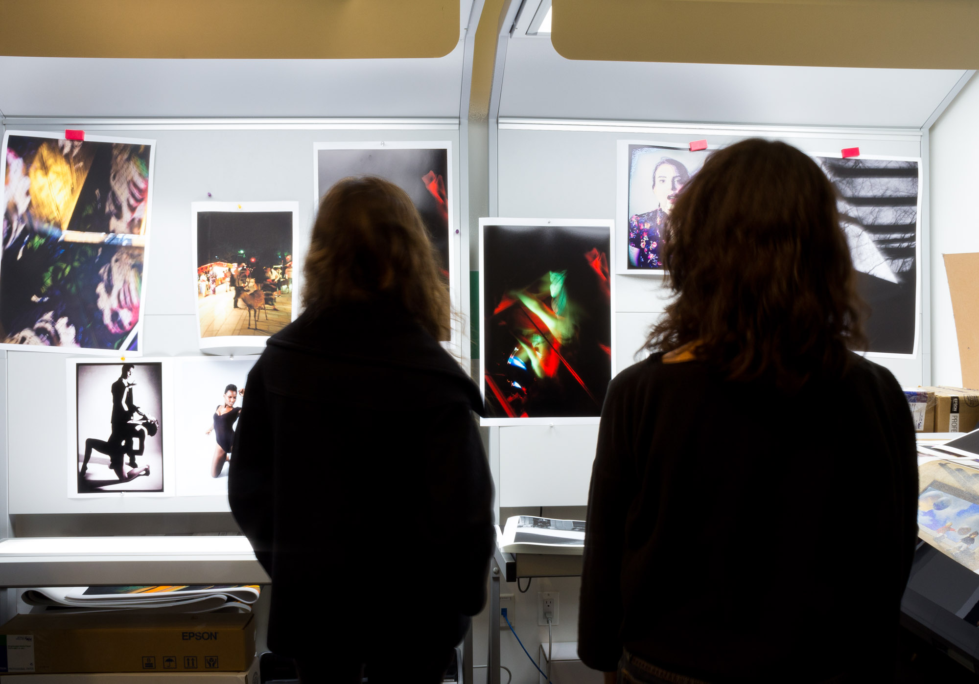 The back view of two SVA students in the print room looking at many prints on the wall.