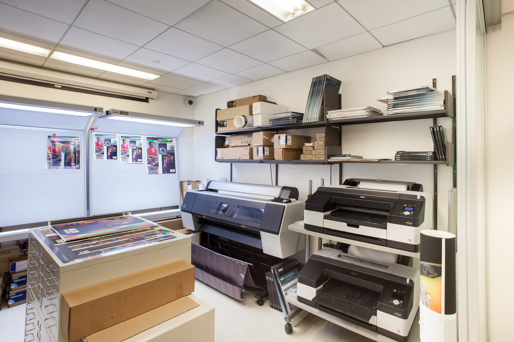 Print room with several prints on the wall in the background and a big printer and several smaller printers.