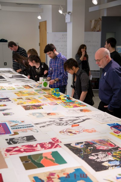 Students work on prints with the supervisor, and many prints are spread on the table.
