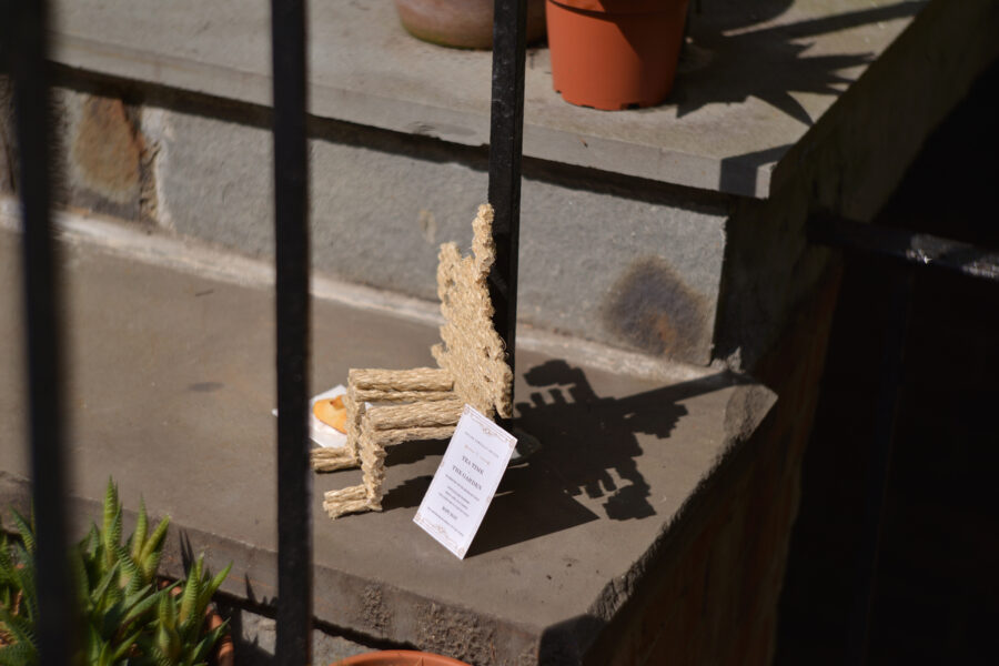 Man made of toothpicks sitting next to plant on steps.