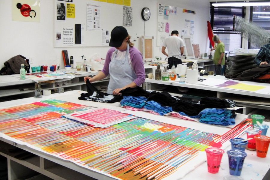 The student works on prints with t-shirts, colors, and other materials.