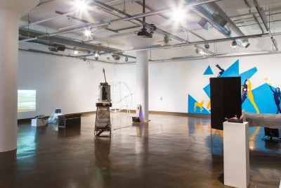 Installation view of sculptures, vinyl art on a wall, and a projected image in the back wall