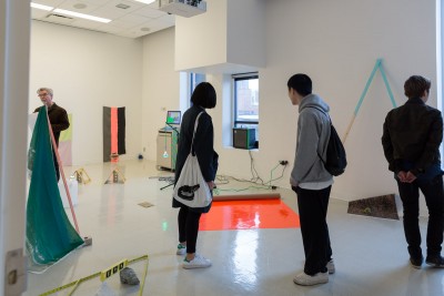 People looking at the installation of artworks with orange vinyl and other sculptures installed on the walls and the floor