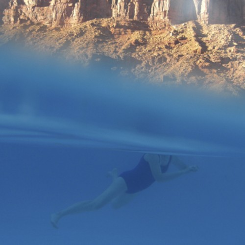 Mountain rocks above the water level and a woman swimming in water in the bottom half of the frame